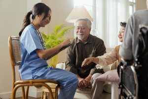 An elderly couple happily receives care information at home from a trained female nurse for a family member who is sitting in a wheelchair.