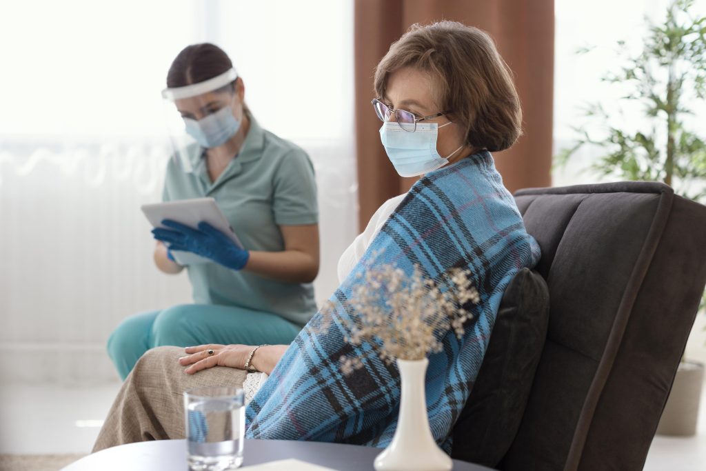 Elderly women sitting on her room sofa next to home care nurse receiving health care and health information details care as part of comprehensive geriatric care.