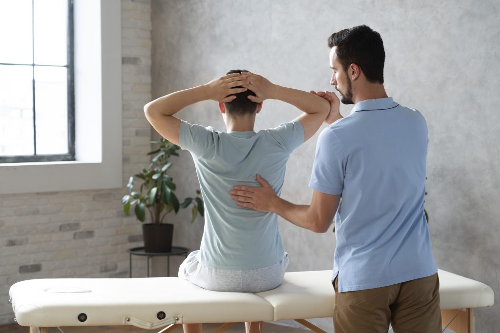 A male physiotherapist helping a young male patient to improve his posture that was caused by a desk job, lifestyle habits, and mobile