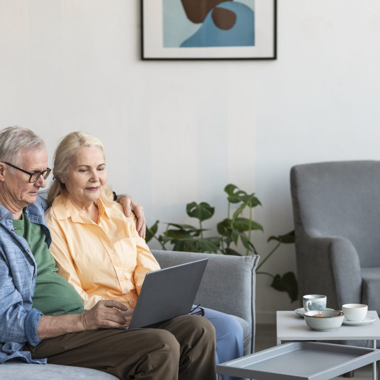An elderly white couple sitting lovingly in their living room and receiving teleconsultation through their laptop screen as part of home health care in dubai